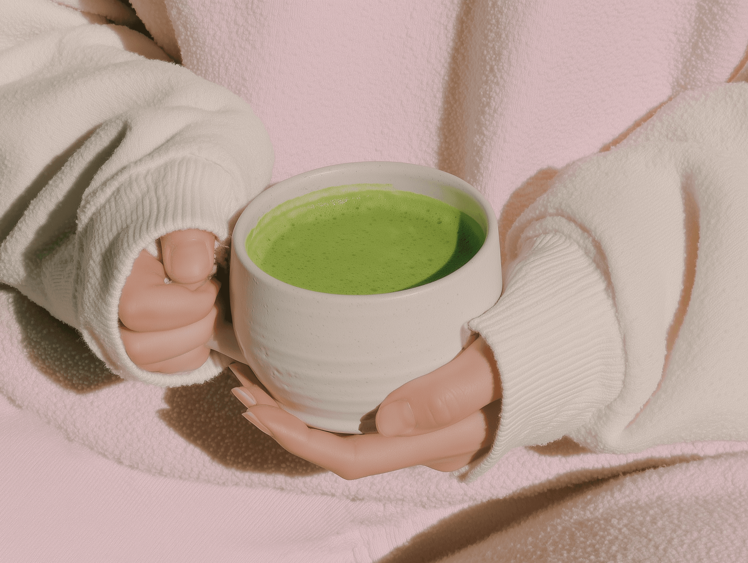 Hands cradling a ceramic matcha bowl with freshly whisked matcha in a cozy white sweater