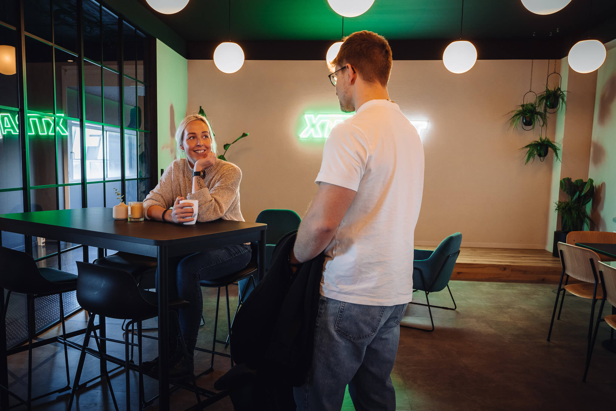 Entspannte Atmosphäre im XTRAFIT Fitnessstudio Büro in Deutschland, wo zwei Mitarbeitende bei einem Getränk eine gesunde Pause genießen. Die Büros sind in einem modernen, industriellen Stil eingerichtet und bieten viele Möglichkeiten für aktive Pausen während der Arbeitszeit.