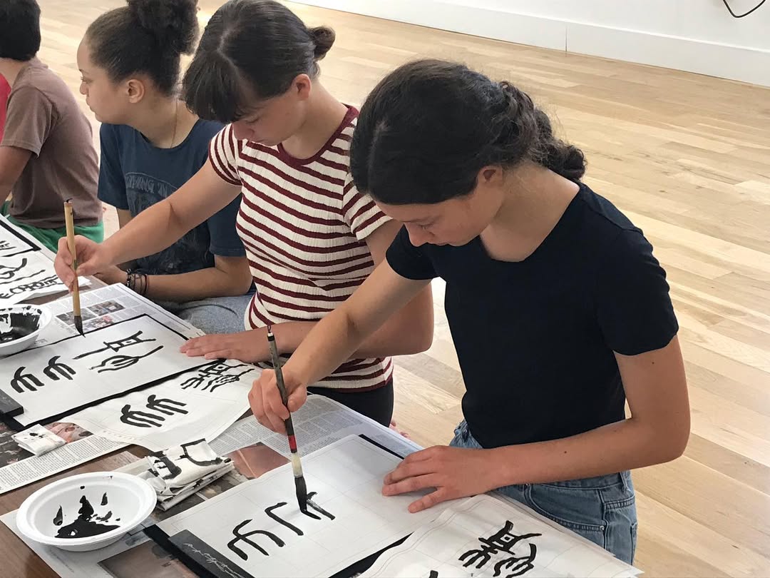 Young woman with short, dark hair and a yellow sweater looks serious, surrounded by hands holding smartphones, conveying intrusion and tension.