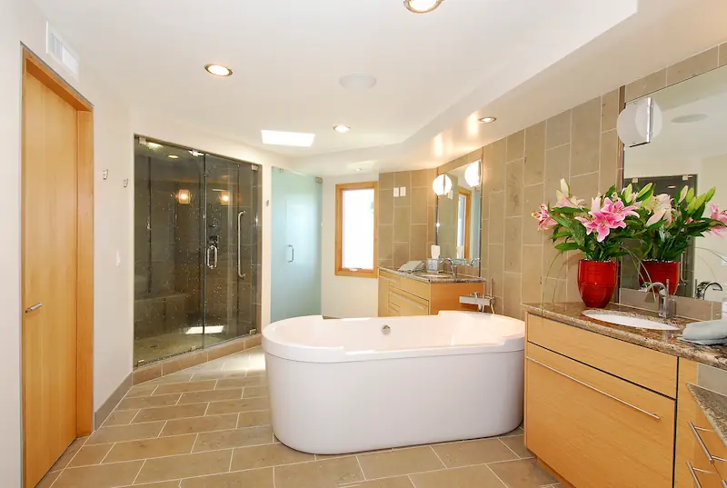 Modern primary bathroom with white free-standing tub, tile flooring, double vanity, recessed lighting, and glass enclosed walk-in shower. Irvine Transitional Modern Project. Photo by Chris Darnall.