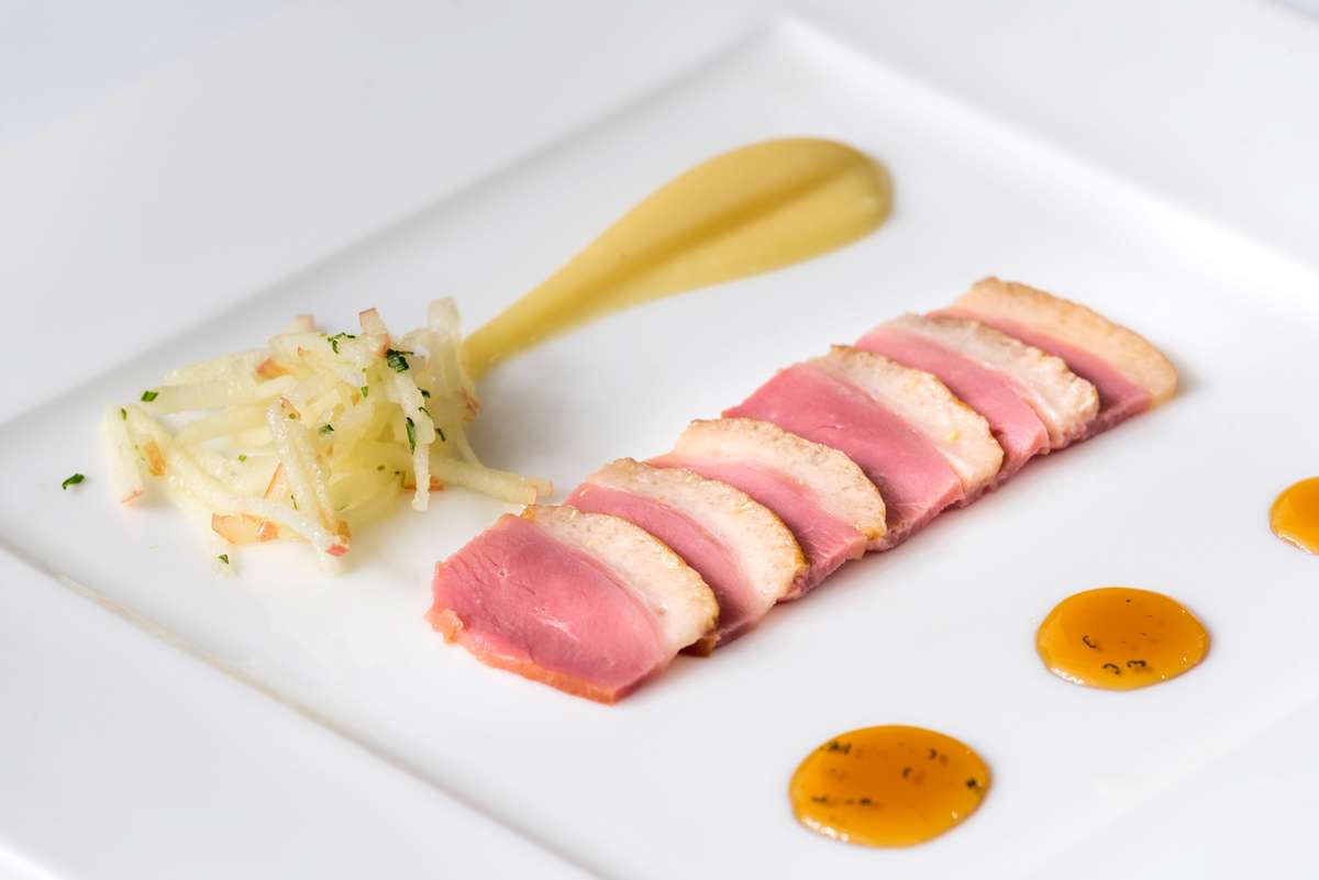 Slices of seared tuna and a pile of julienned vegetables are served on a white plate with yellow and orange sauces.