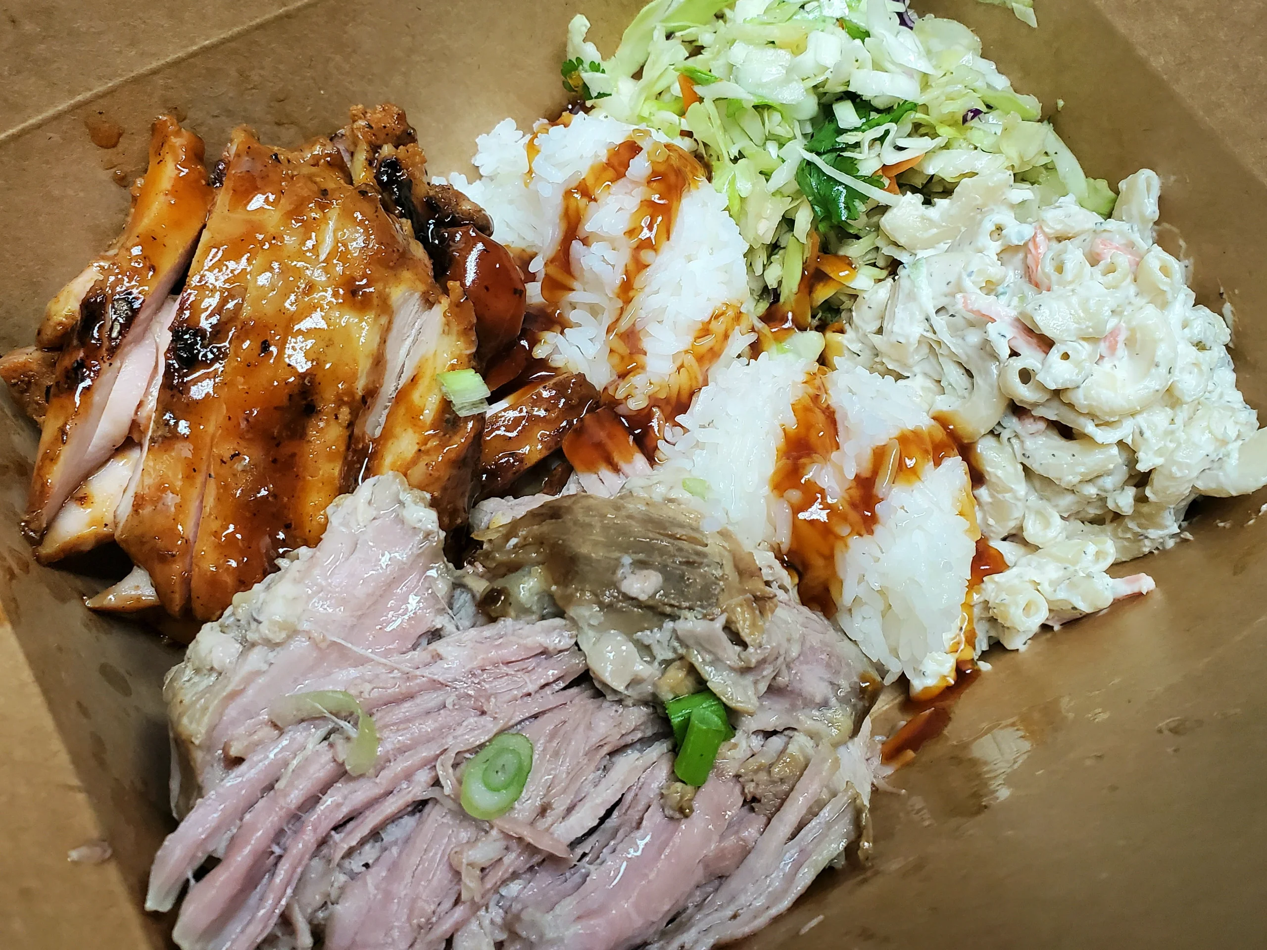 A large Hawaiian BBQ combo plate featuring a pile of shredded Kalua pork, sliced char-grilled Huli Huli chicken, two scoops of rice, mac salad, and slaw.