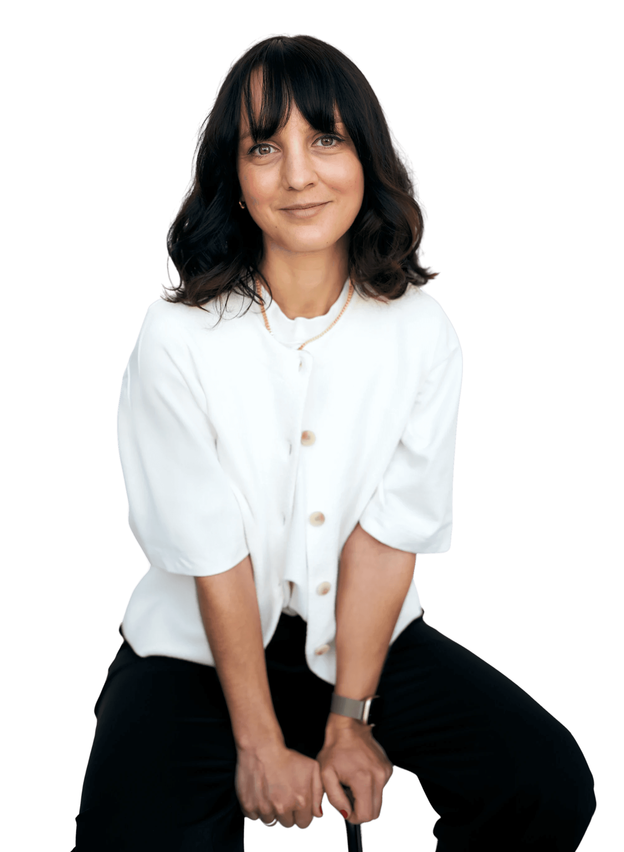 A young person with curly hair smiles at the camera while sitting in front of a laptop against a dark background.