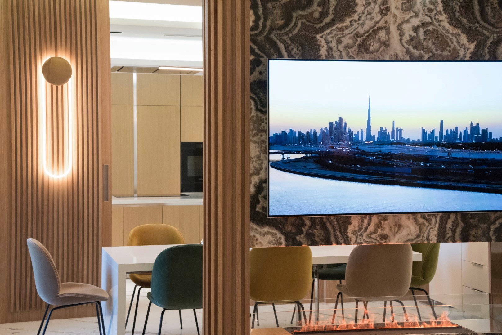 A modern living room features a wall-mounted TV displaying a cityscape view with a prominent skyline, alongside a sleek fireplace and contemporary furniture under soft ambient lighting.
