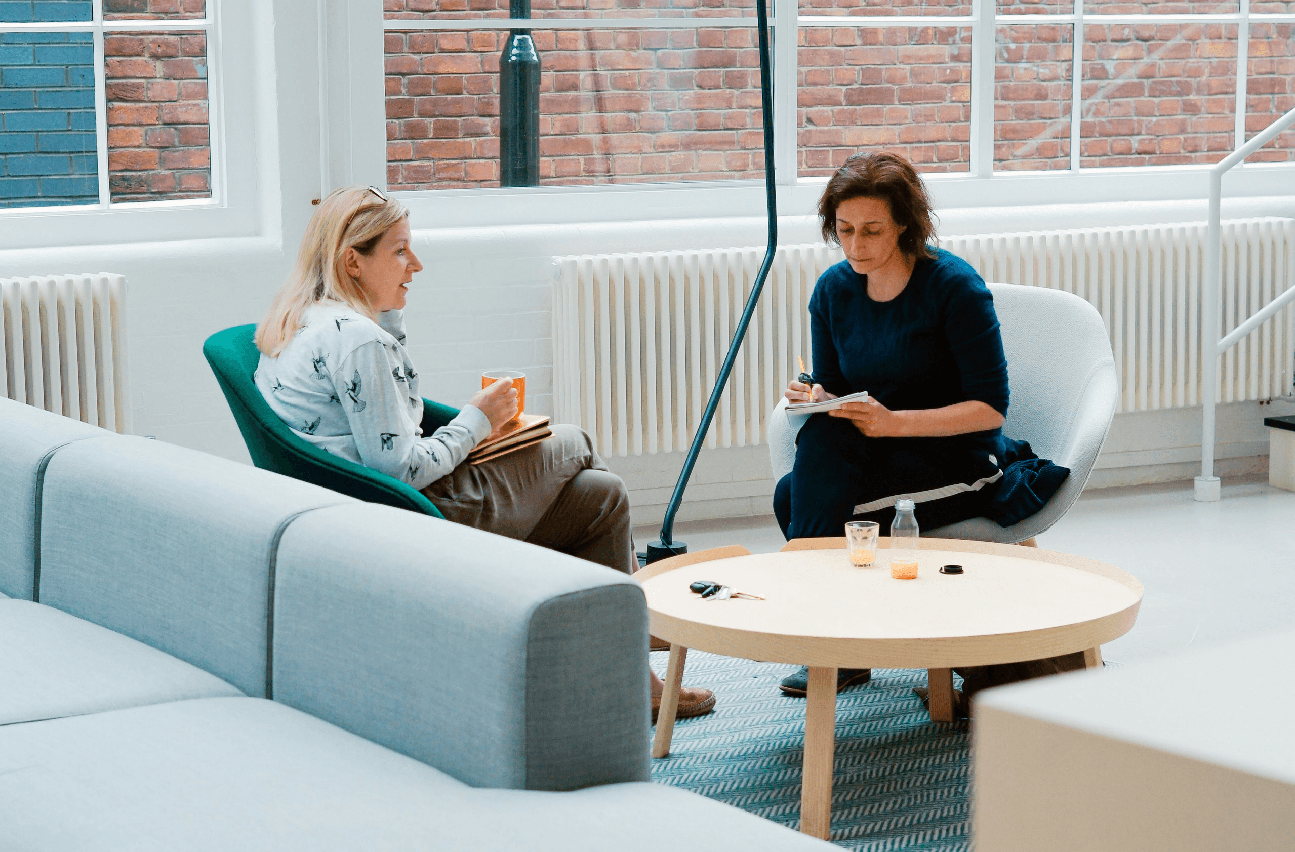 two woman sits on sofa chairs inside house