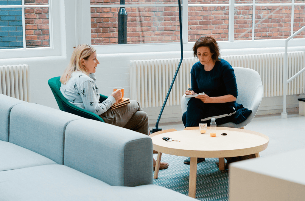 two woman sits on sofa chairs inside house