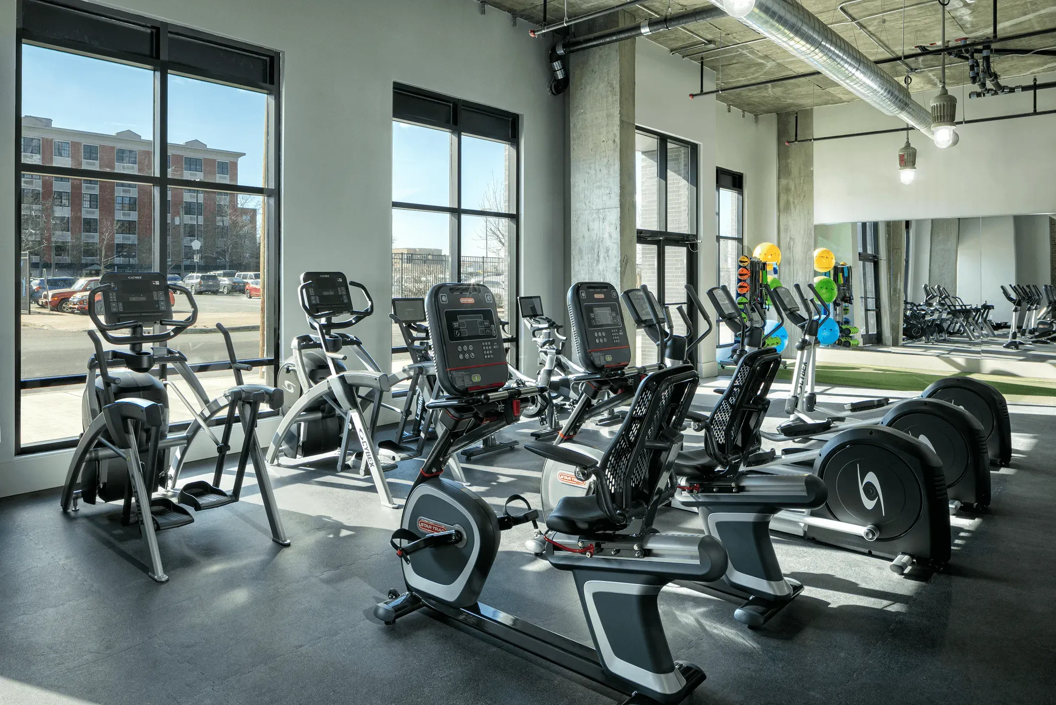 A bright, modern gym interior featuring various workout equipment and large windows letting in natural light.