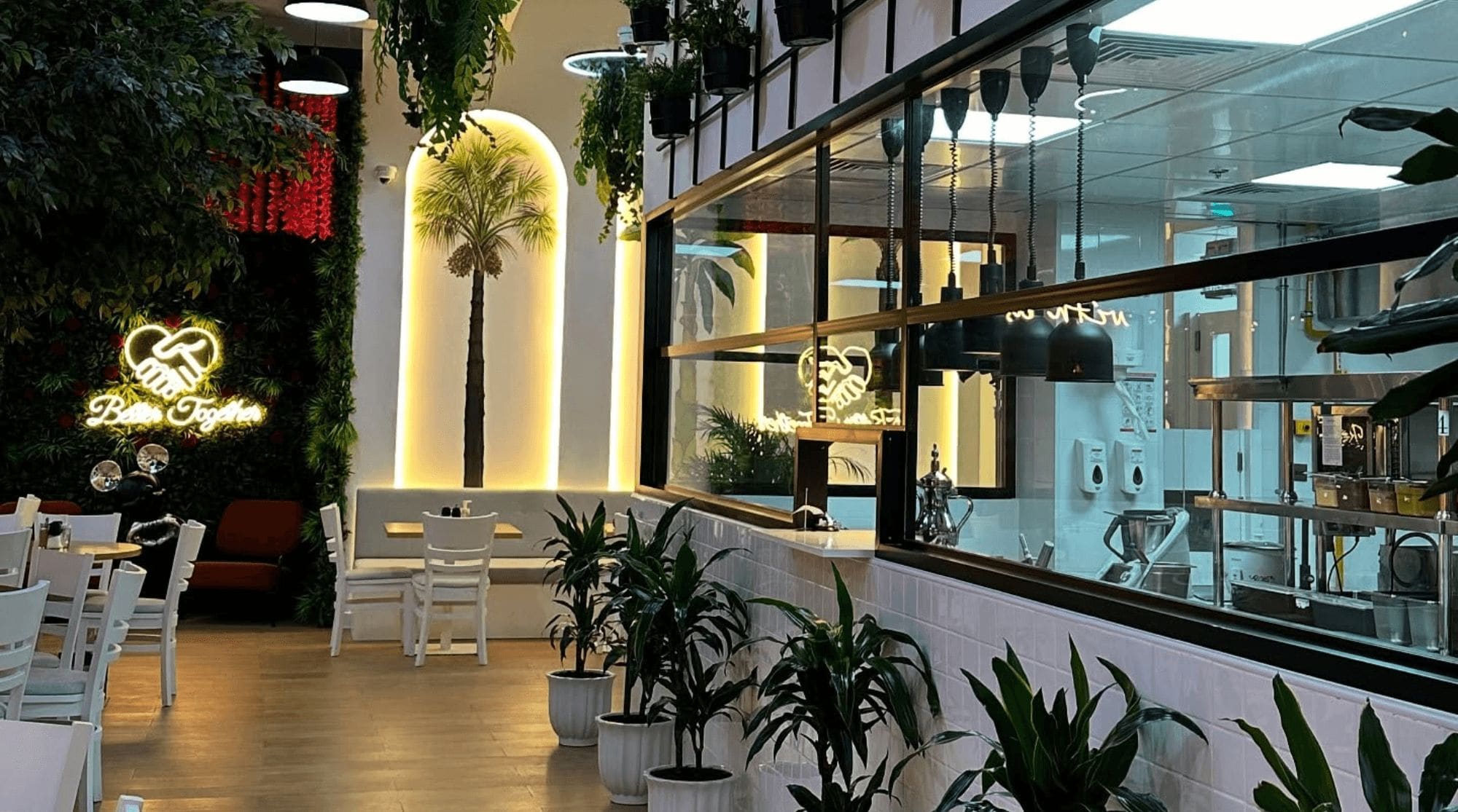 A breakfast place in Dubai that features open kitchens, greenery, white chairs, and wooden dining tables. 
