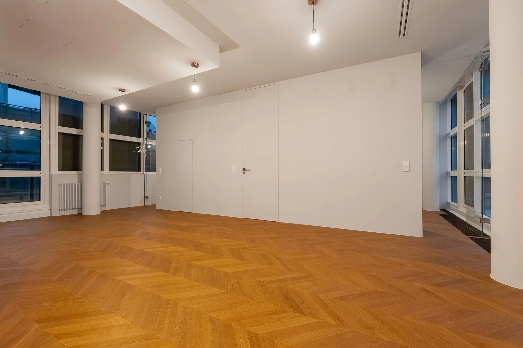 Großzügiger Wohnbereich mit frisch verlegtem Chevron-Parkettboden und modernen Einbaulampen.