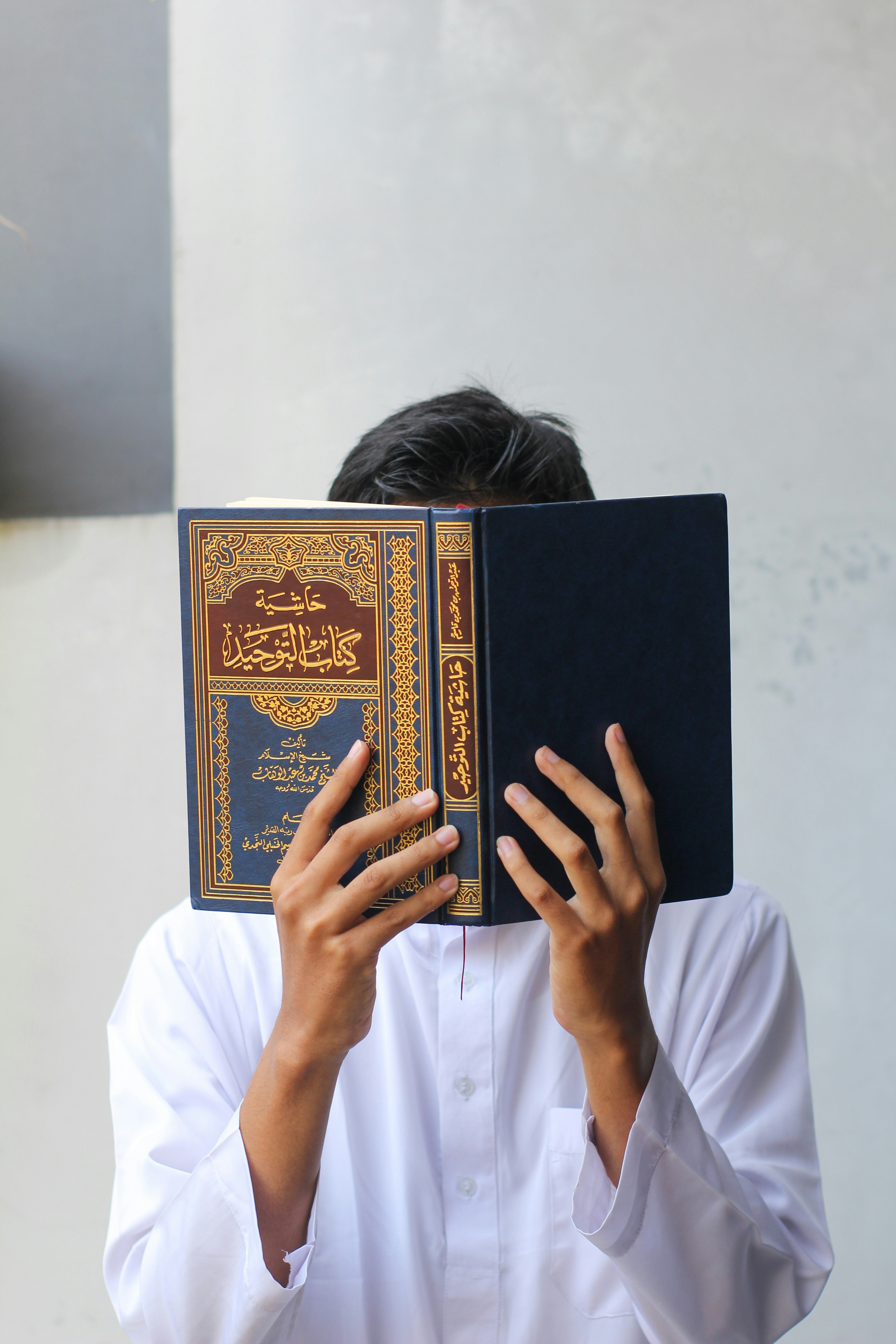 Person in white clothing holding up a blue and gold Islamic book.