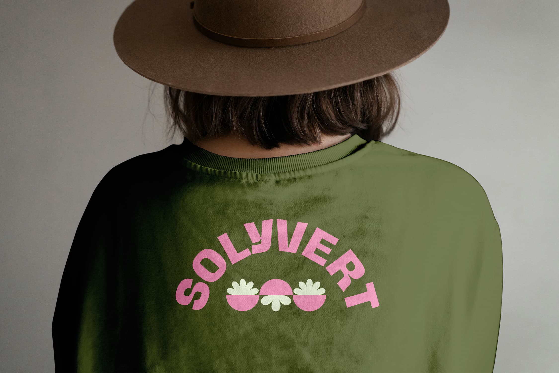 Woman wearing a green Solyvert T-shirt with a roundel logo back print and a brown hat.