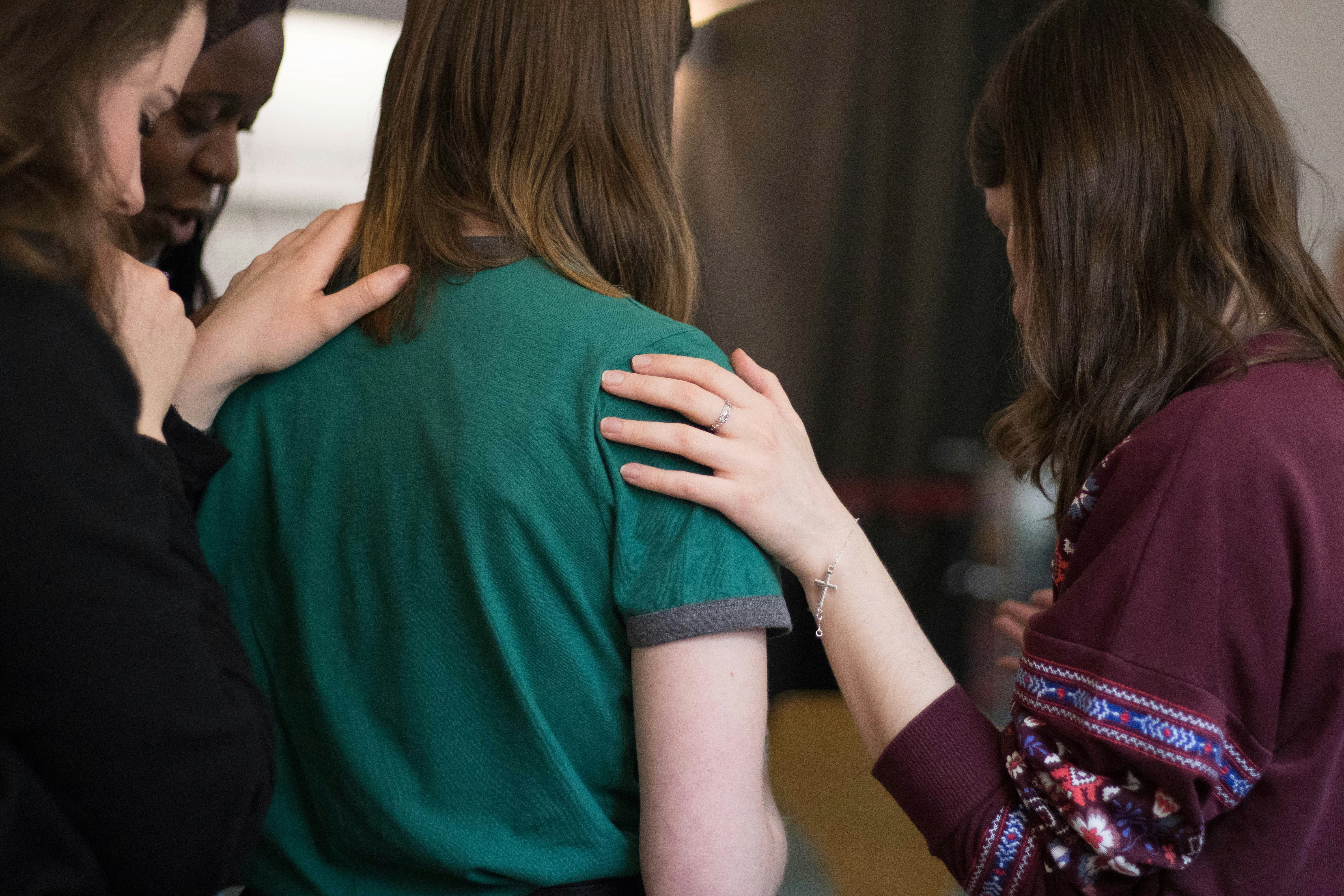 Conversion Truth for Families - 4 young women placing their hands on the back of a woman in a green top.