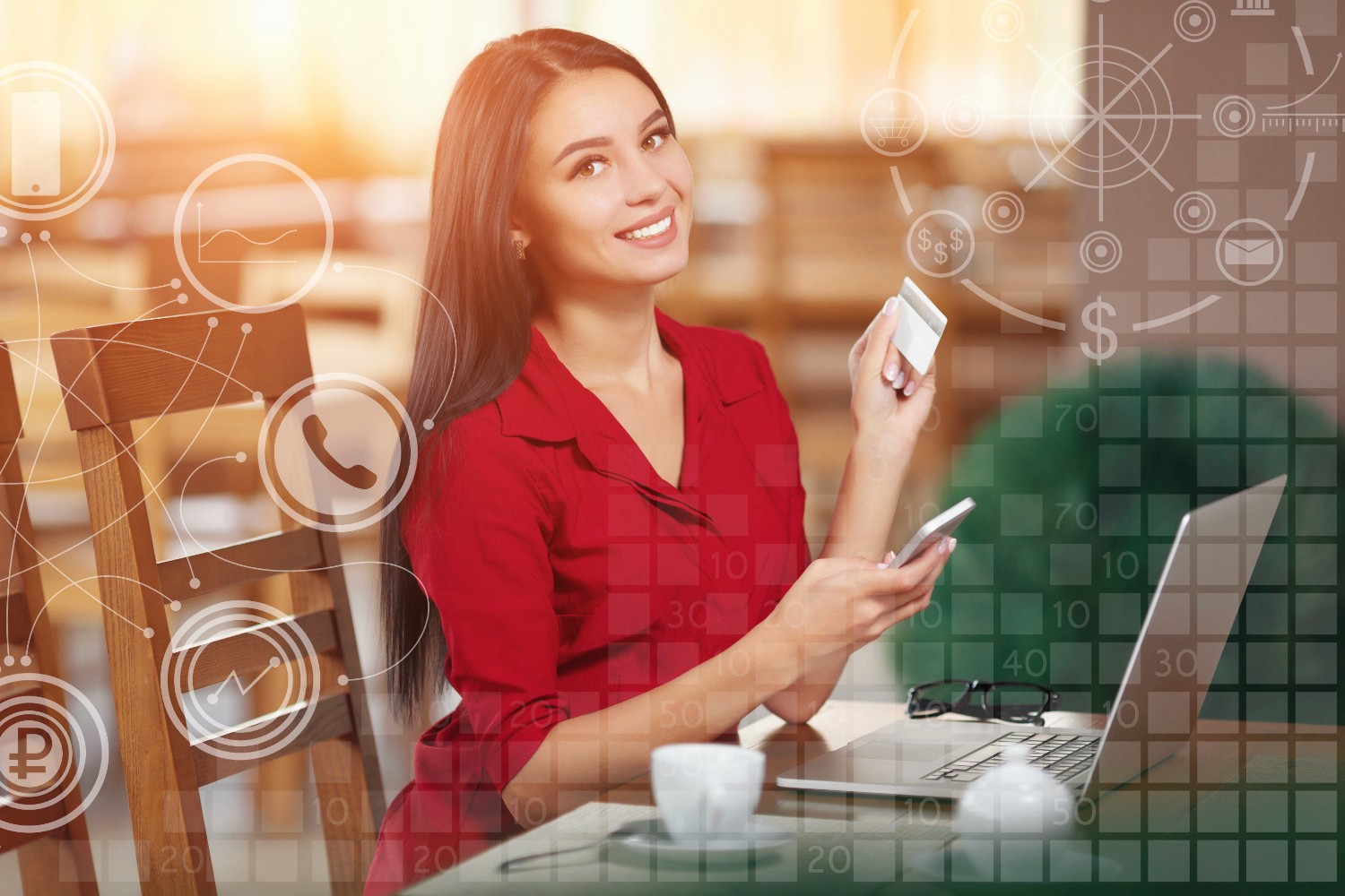 A woman seated at a table, using a laptop while holding a credit card in her hand.