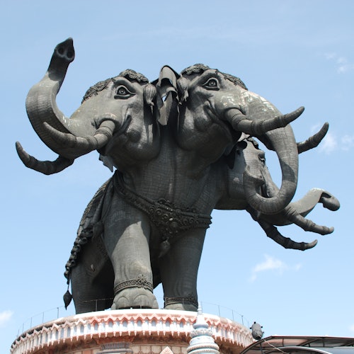 在晴朗的蓝天下，一座带有华丽细节的三头大象雕像矗立在装饰底座上。