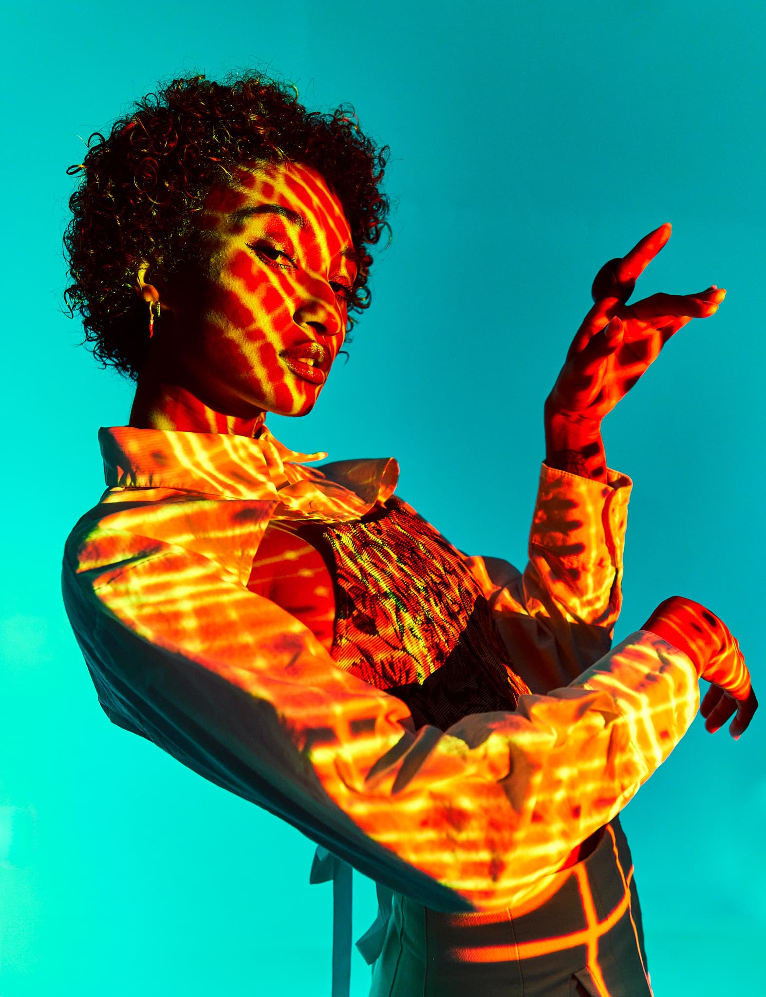 A model strikes a dynamic pose with red and yellow light patterns projected against a blue background at Revelator Studio, a photography studio in Shreveport.