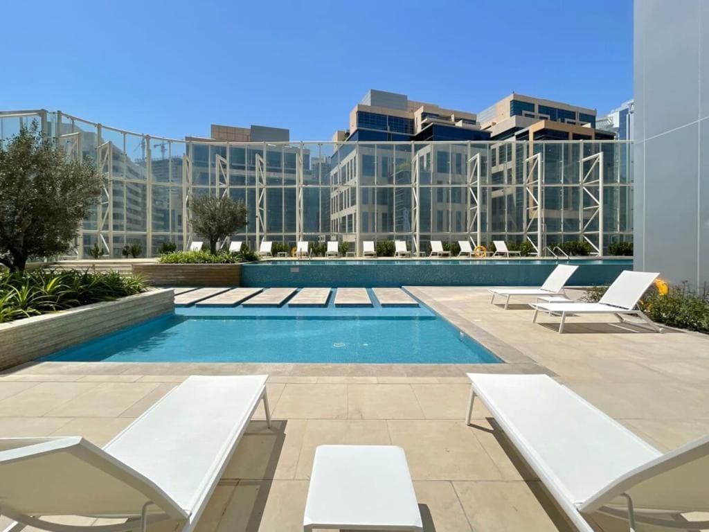 A pool surrounded by lounge chairs and a glass wall at The Pad by OMNIYAT, showcasing a modern, luxurious setting.