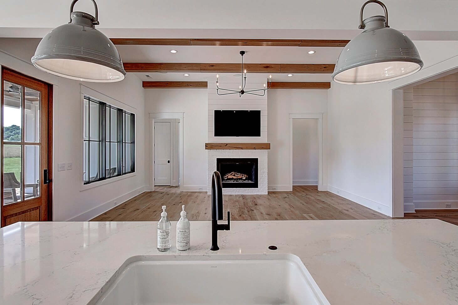 A modern kitchen with a central sink, wooden beams, and white cabinets, featuring an open layout and natural light.
