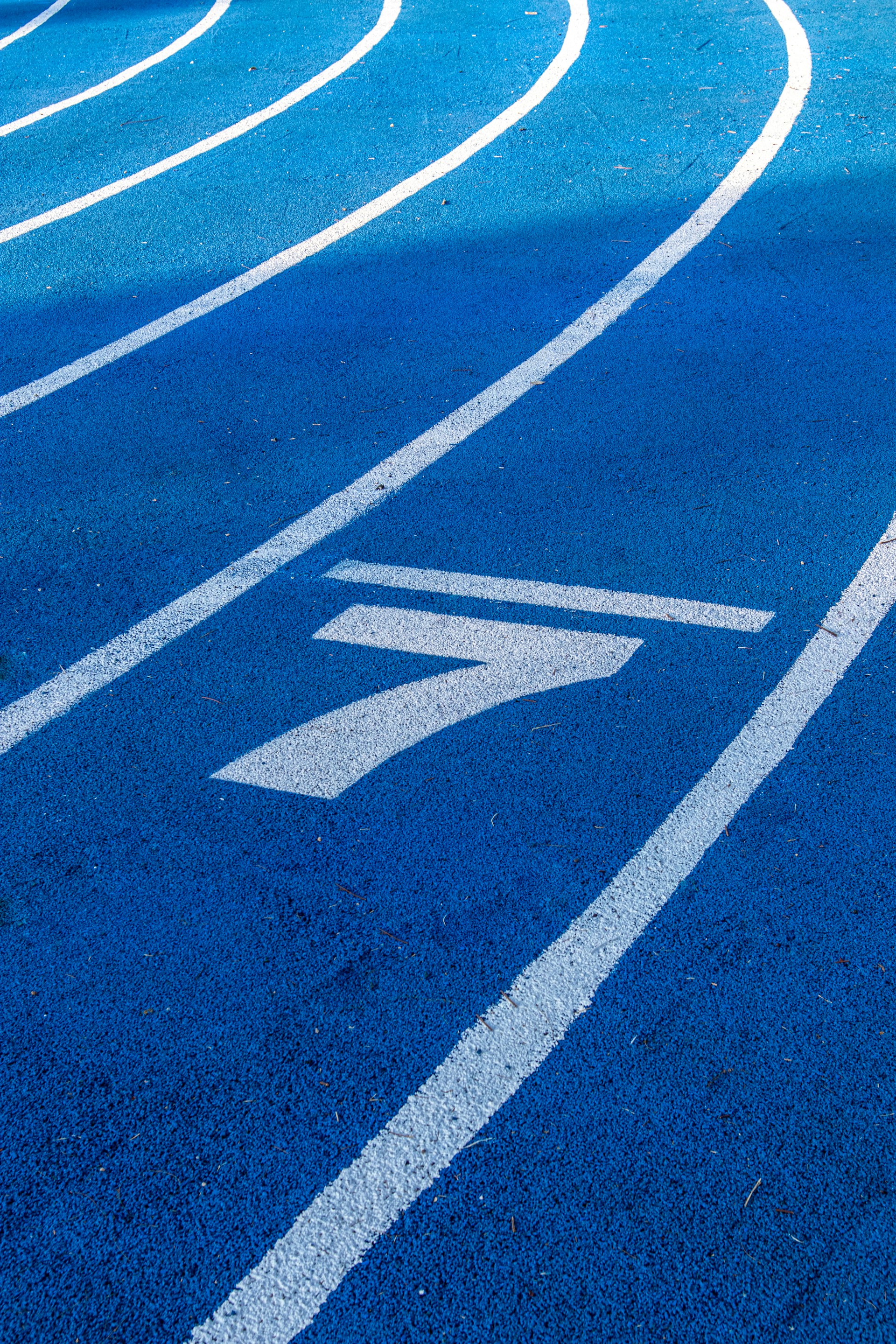 High-angle view of a blue running track lane painted with a large white number "7".