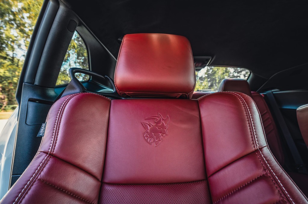 The image shows a sleek, red leather car seat with a black leather interior and a subtle emblem, suggesting a luxury vehicle with a spacious and stylish interior.
