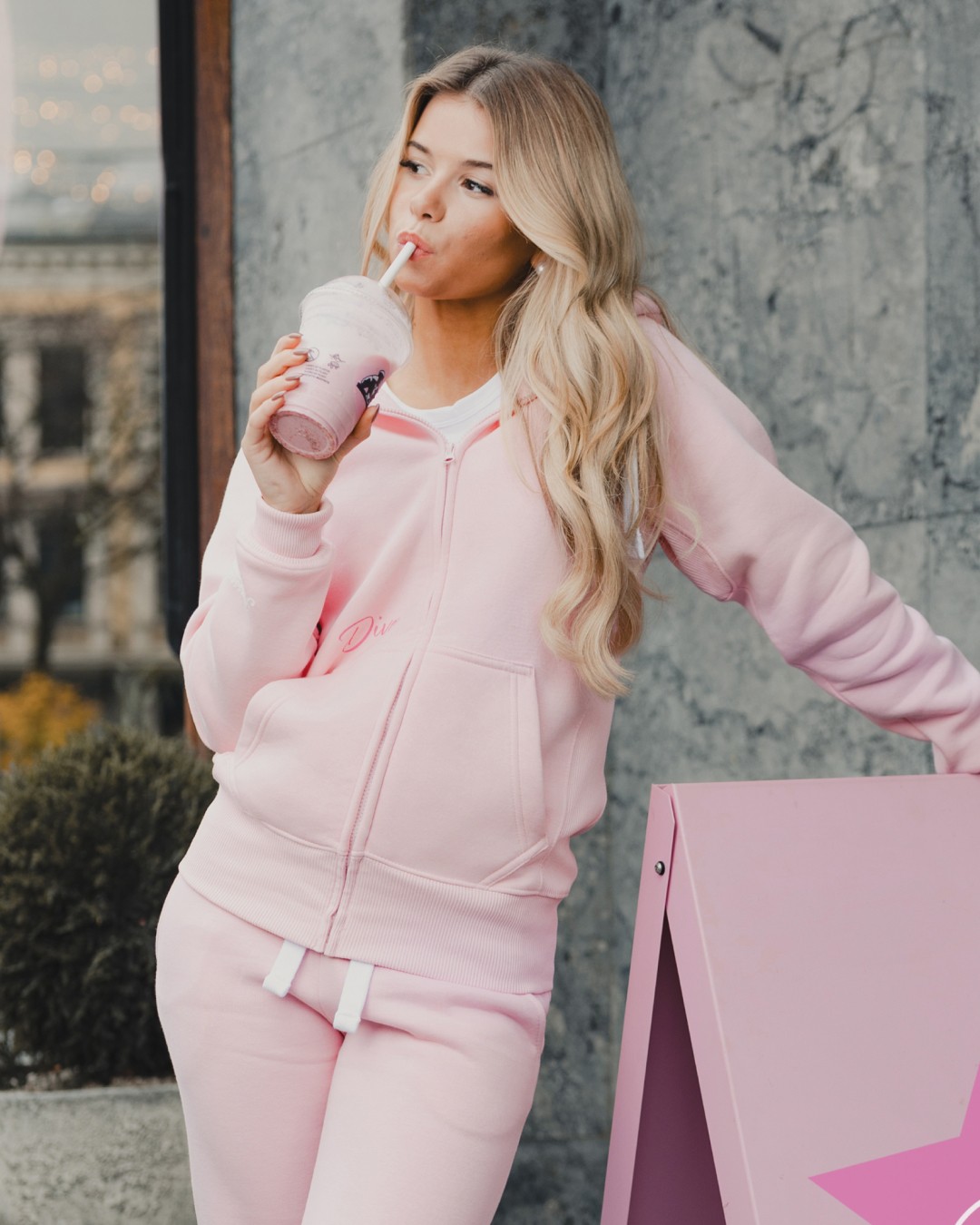 Girl wearing a pink sweatsuit and drinking a pink smoothie in an urban setting