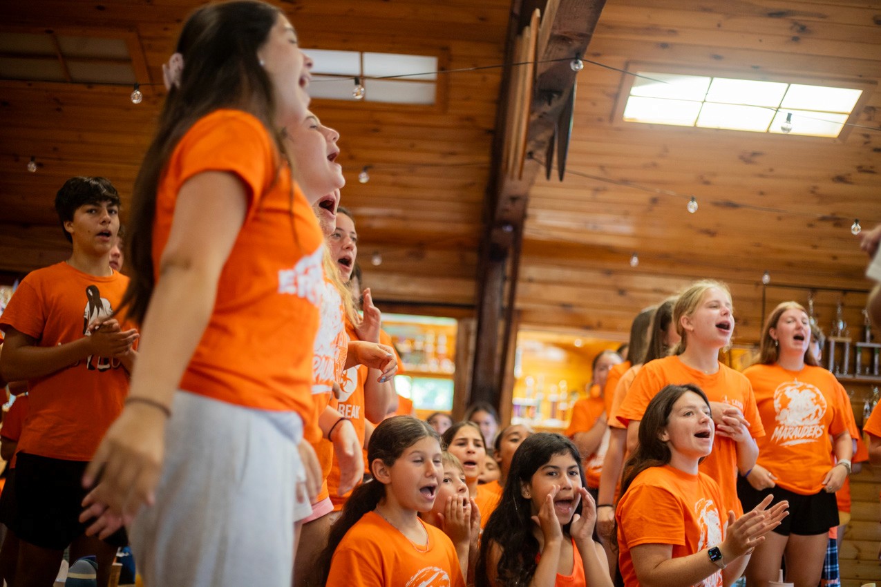 Campers in orange shirts cheering in the dining hall at Camp Lenox