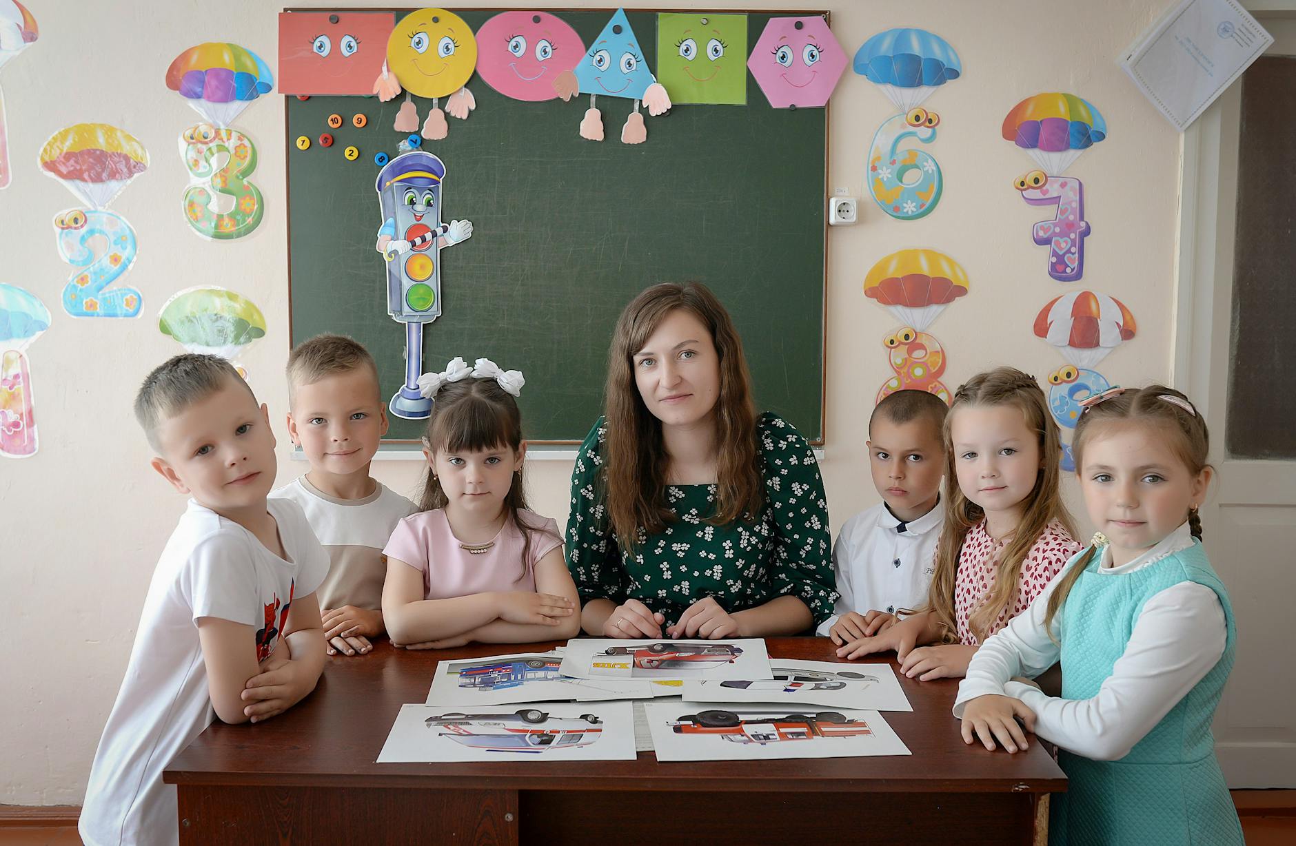 Elementary students sitting on a rug listening to a teacher holding an iPad in a bright classroom.