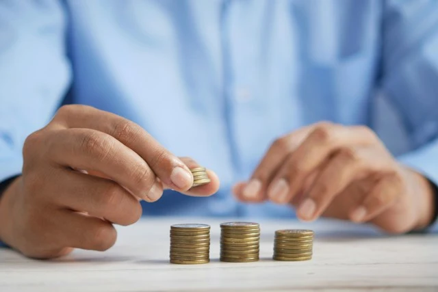 Manos apilando monedas en montones crecientes sobre una mesa, representando el ahorro acumulado en un plan de pensiones antes de decidir su rescate a los 10 años