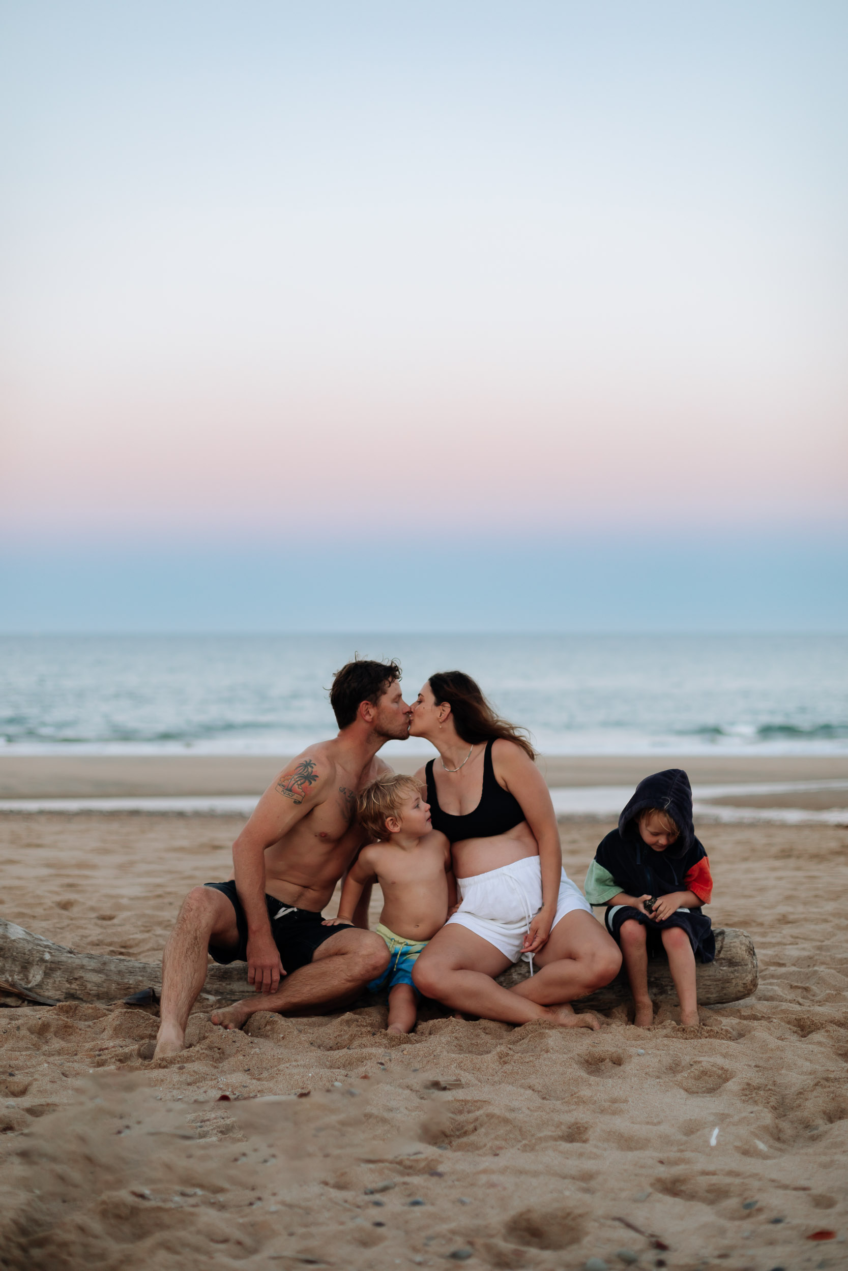 Family sitting on surfboard at sunset on the beach in Mackay