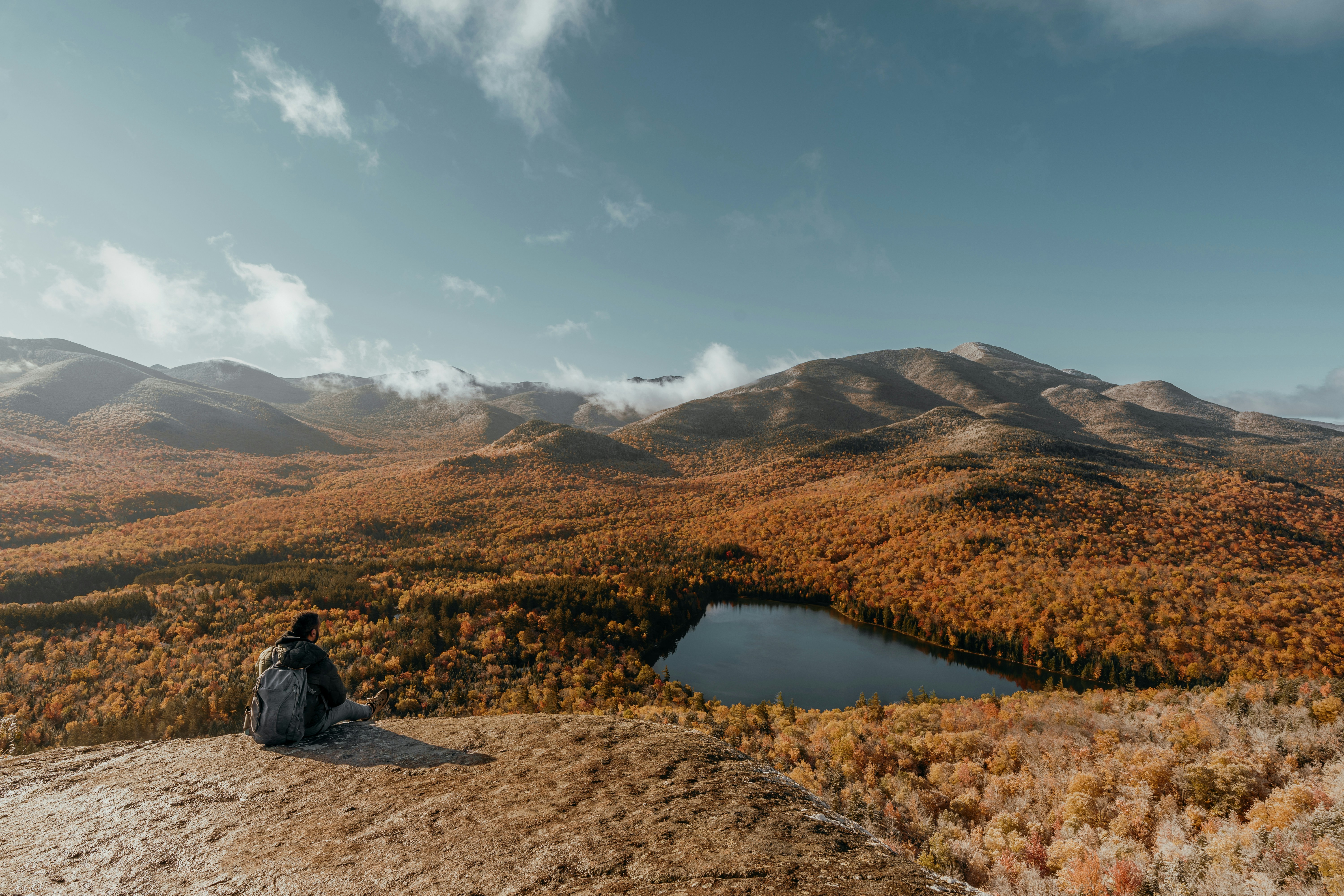 a person sitting on a rock looking at a lake surrounded by mountains