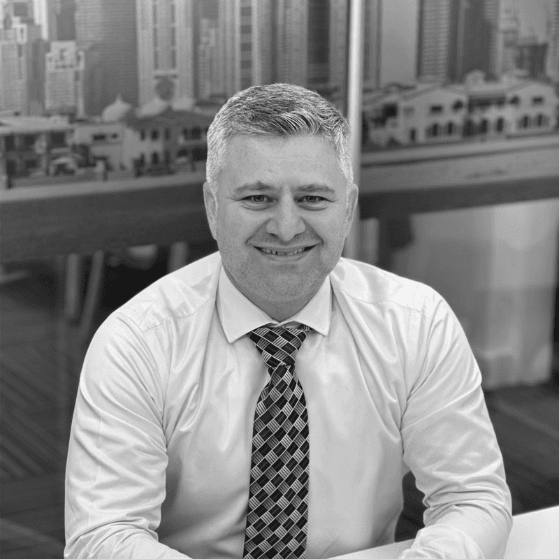 A man standing in a modern studio space, gesturing while discussing architectural plans. Shelves with books and models line the background.