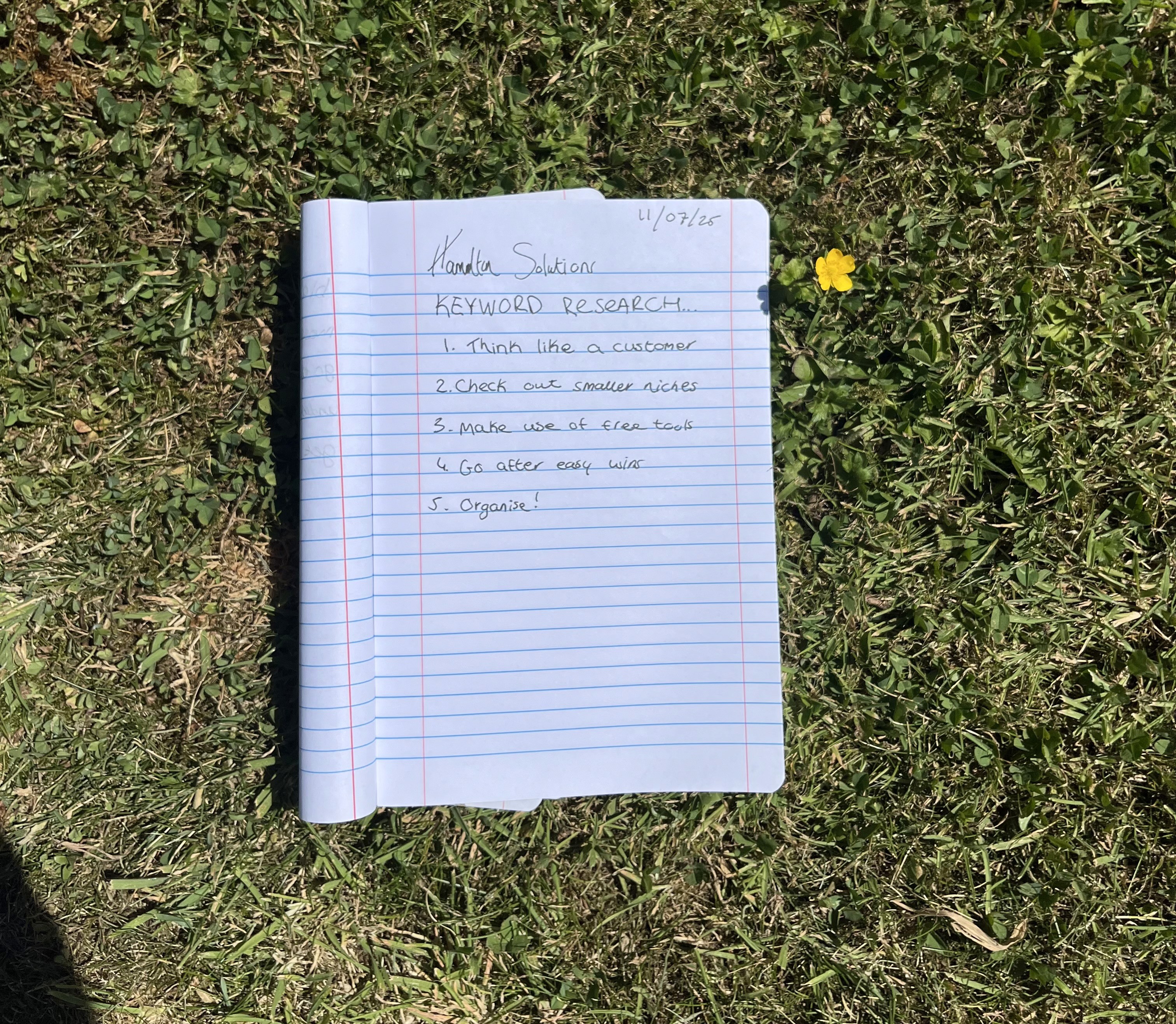 a copybook sitting in the grass that gives tips on keyword research by hamilton solutions