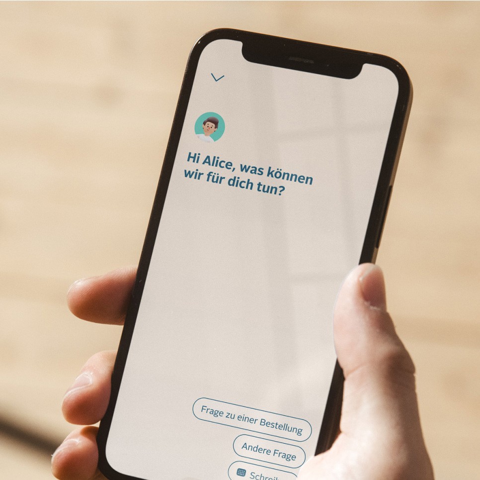 Detailed view of a hand and a smartphone. Person holding smartphone in right hand. Chat bot: "Hi Alice, what can we do for you?" Three possible answers are listed below.