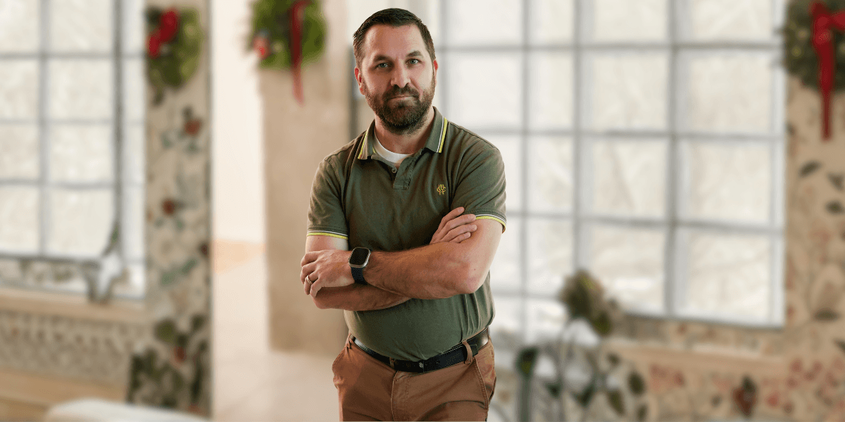 Joshua Polivka standing confidently with arms crossed in a green polo shirt, set against a holiday-themed backdrop.