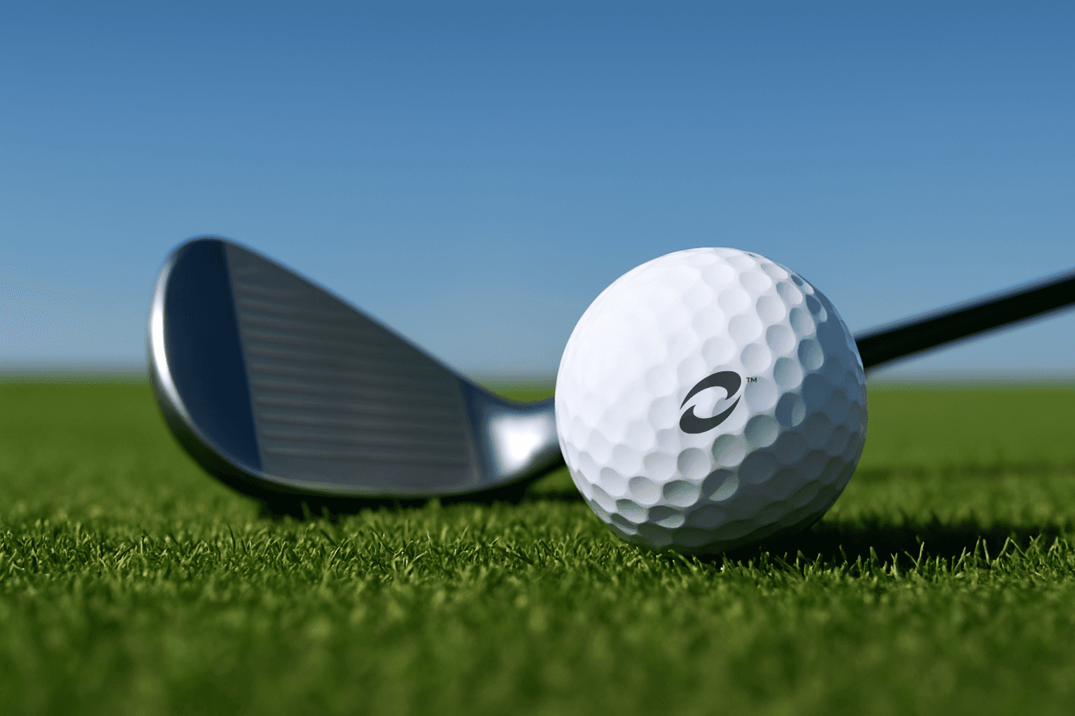 Close-up of a golf ball on green grass with a golf club behind it under a clear blue sky.