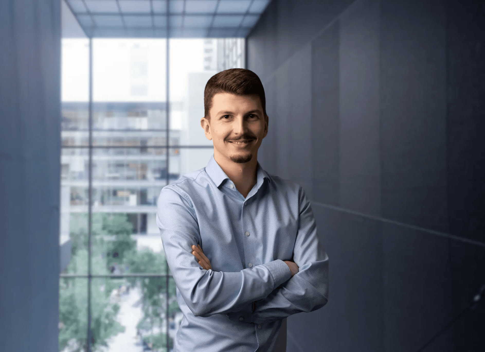Junger Geschäftsmann mit verschränkten Armen in modernem Bürogebäude