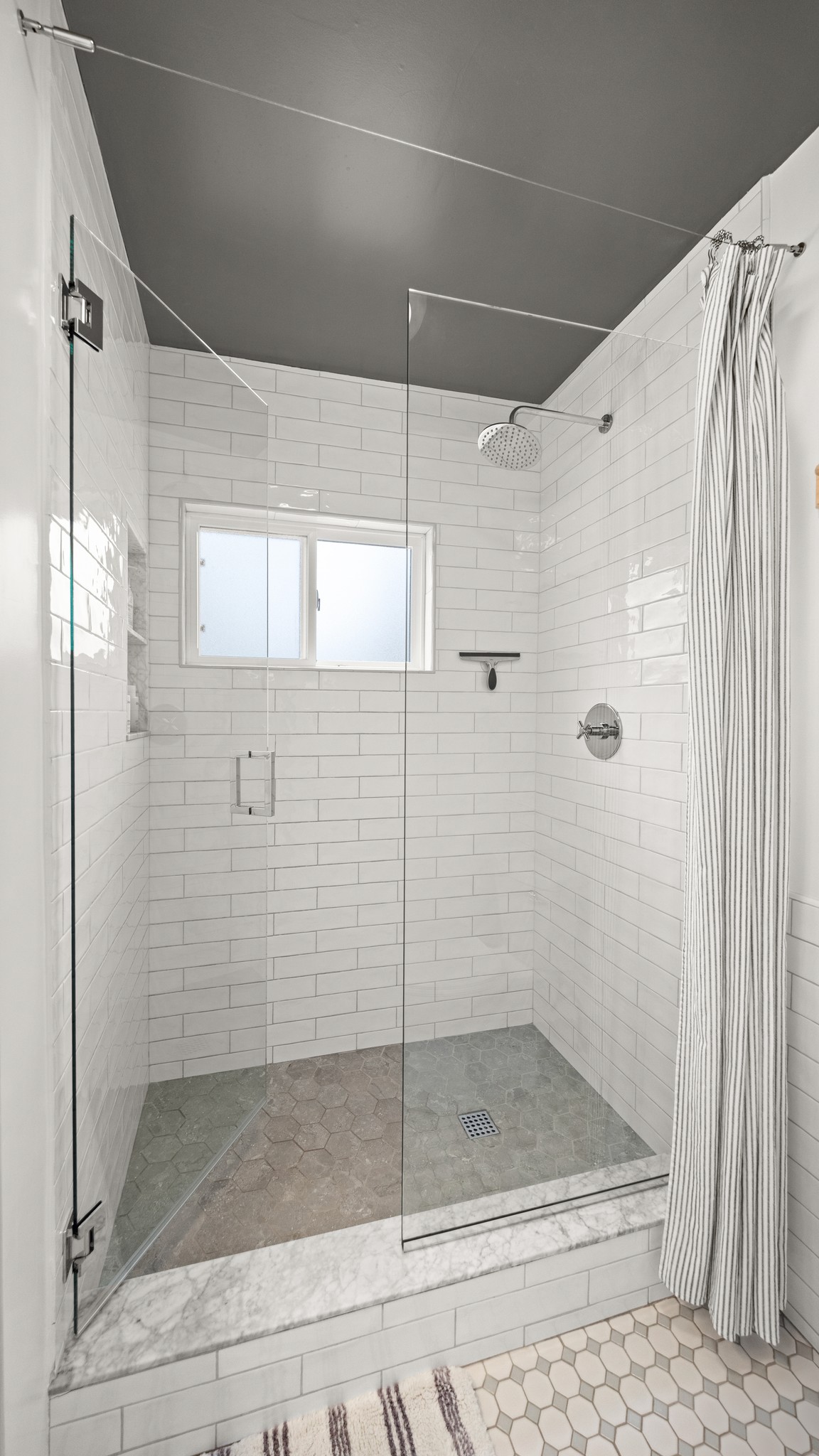 A spacious, spa-style walk-in shower featuring classic subway tile, a rainfall showerhead, and marble detailing.