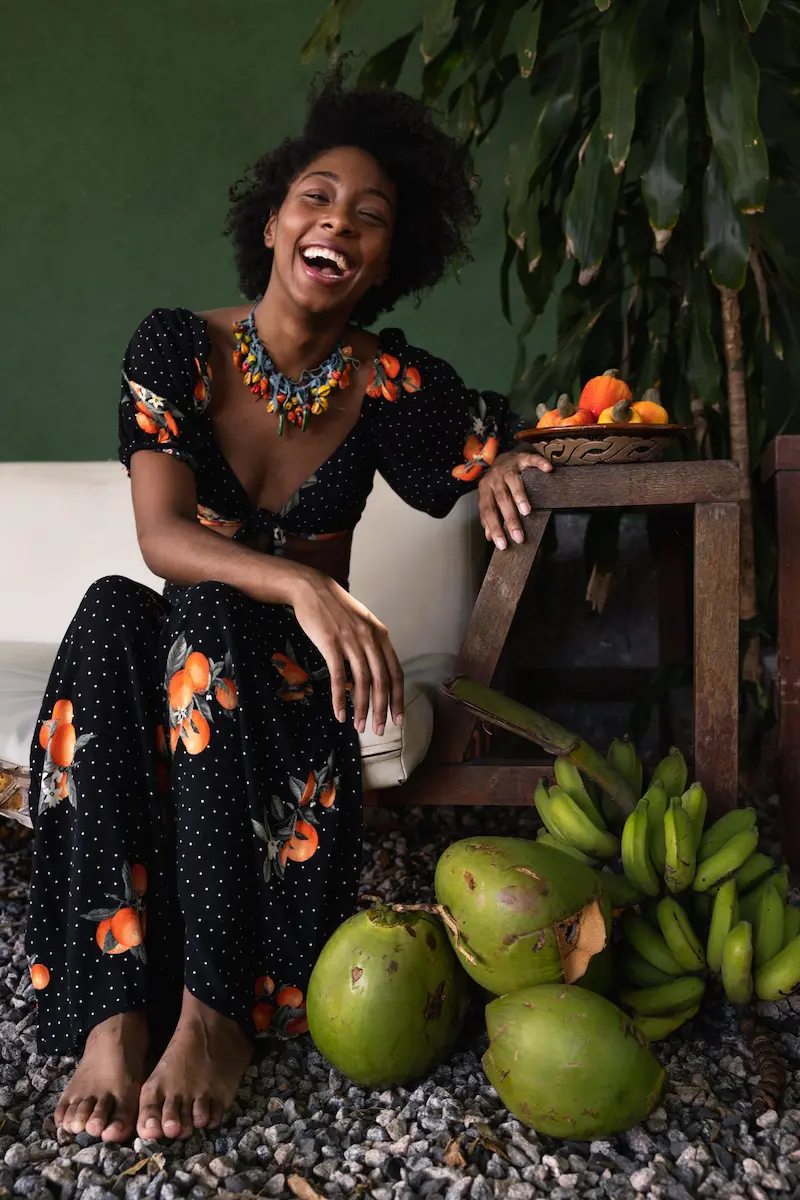 Femme souriante en robe fleurie posant avec des fruits tropicaux