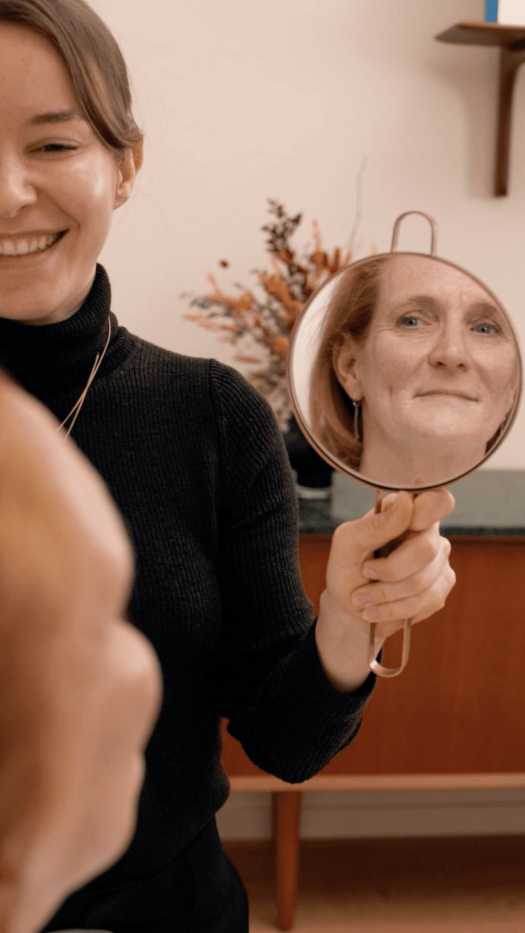 Hand holding a piece of broken mirror reflecting a woman's image, with the blue sky in the background.