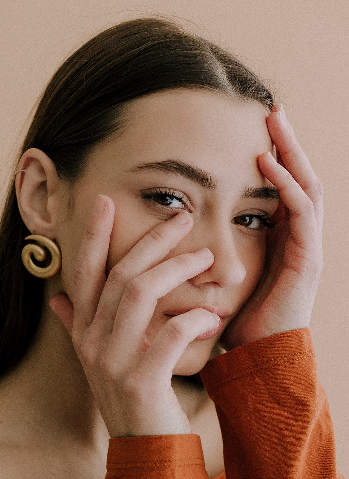 A close-up of a model cradling her face, with gold accessories, photographed in the natural light at Revelator Studio, Shreveport’s premier photography studio.