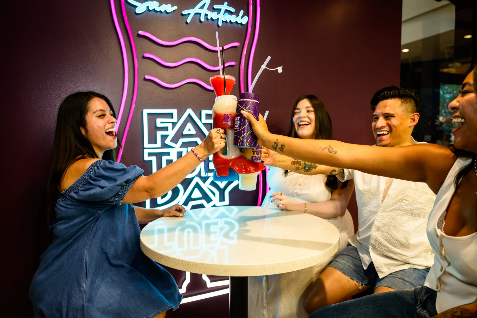Group of friends toasting layered frozen daiquiris beneath the neon Fat Tuesday San Antonio sign