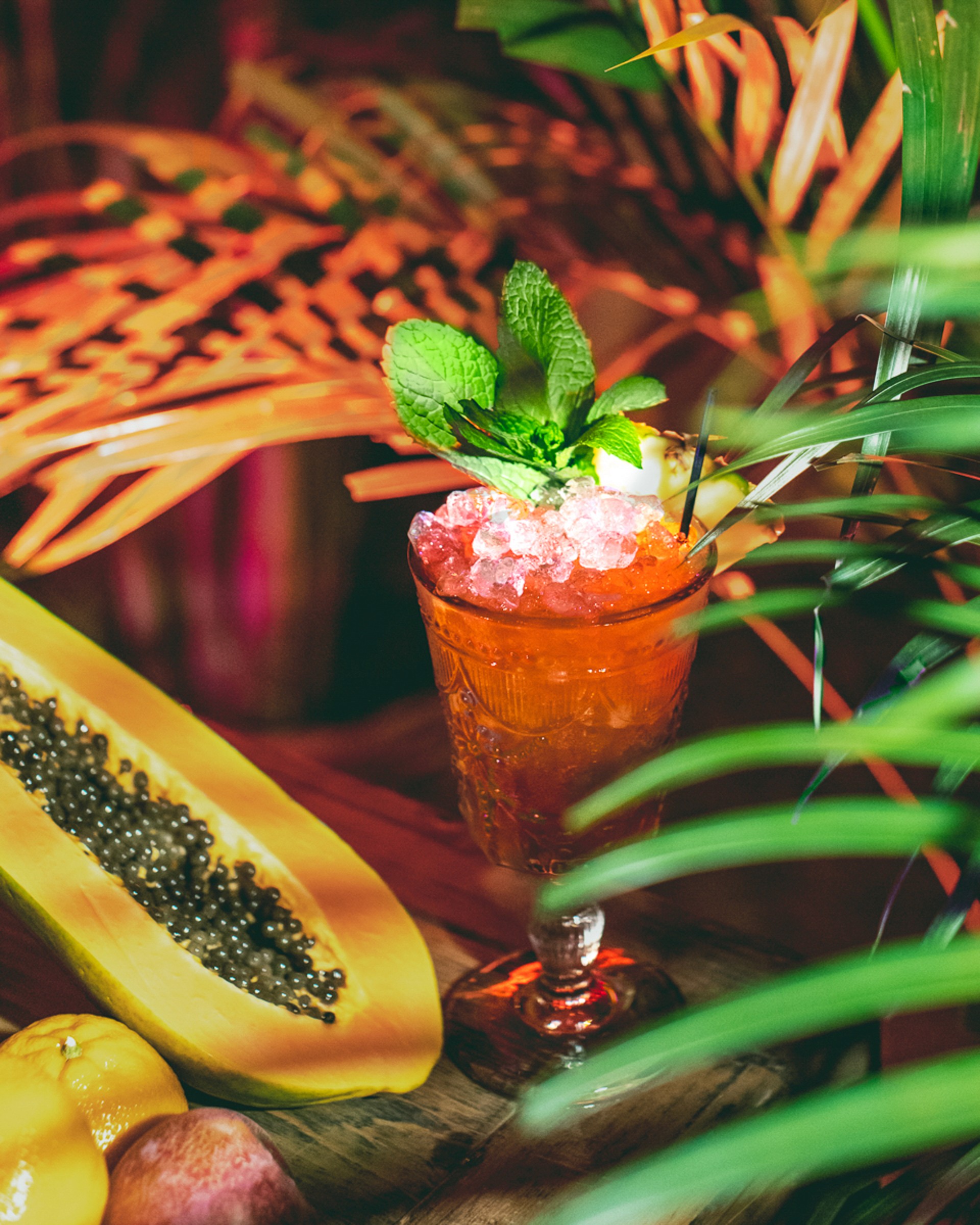 A cocktail garnished with mint and papaya, served in a decorative glass