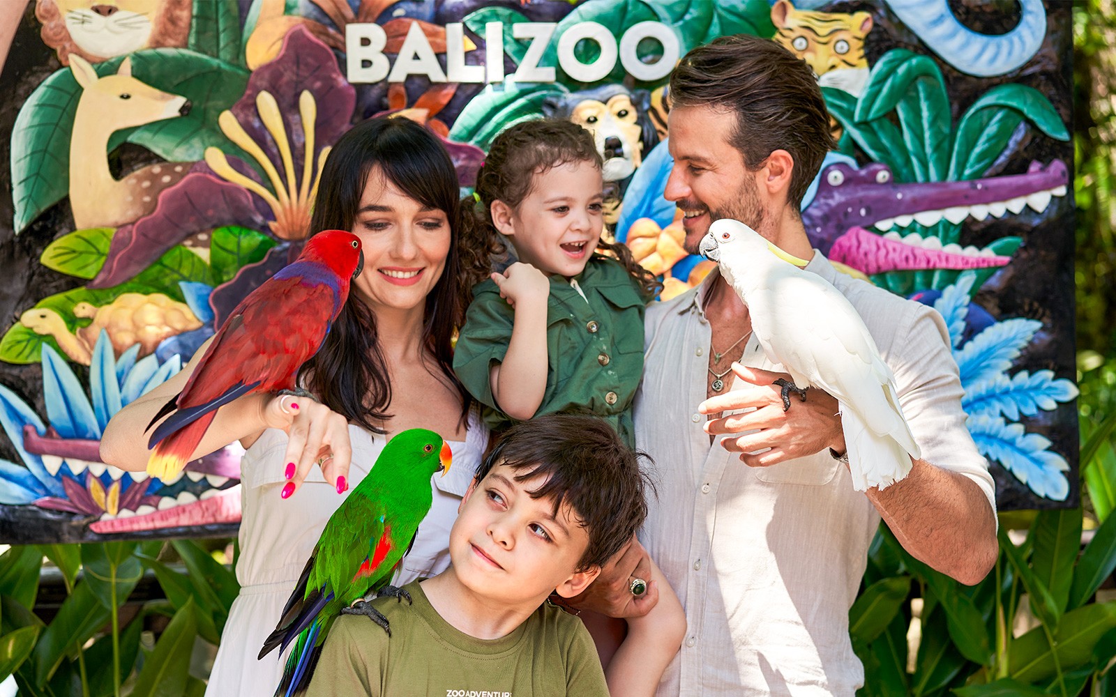 Family enjoying colorful parrots at Bali Zoo entrance.