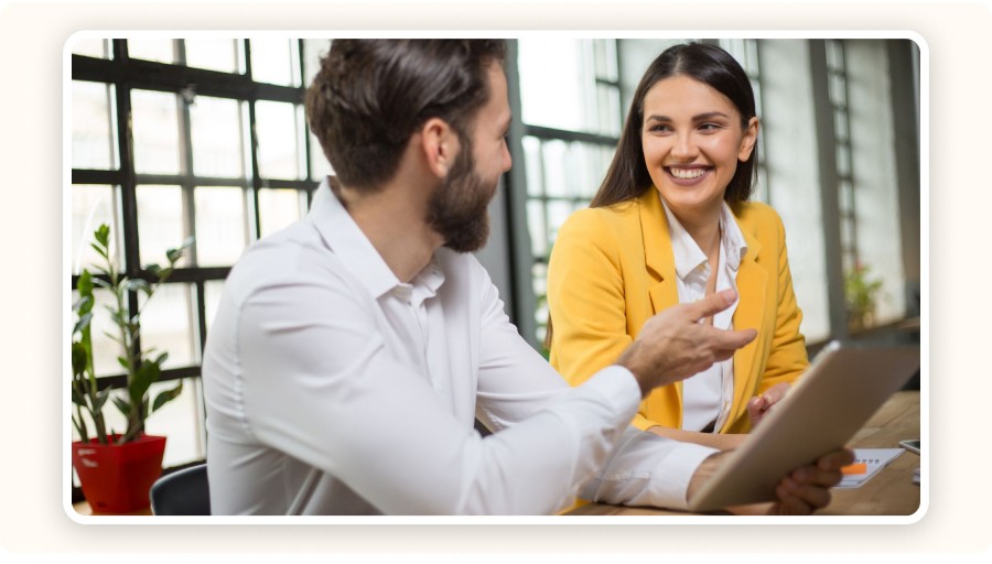 Two colleagues smiling, discussing work together on tablet in office