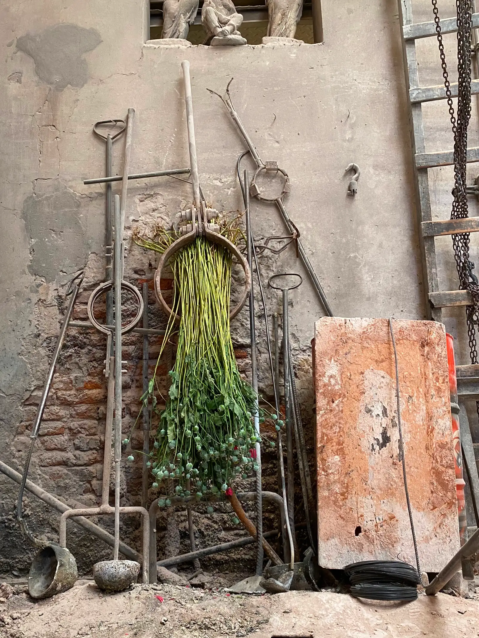 Escena de taller con herramientas y ramo verde suspendido para creadores que trabajan con materiales reciclados y procesos escultóricos.