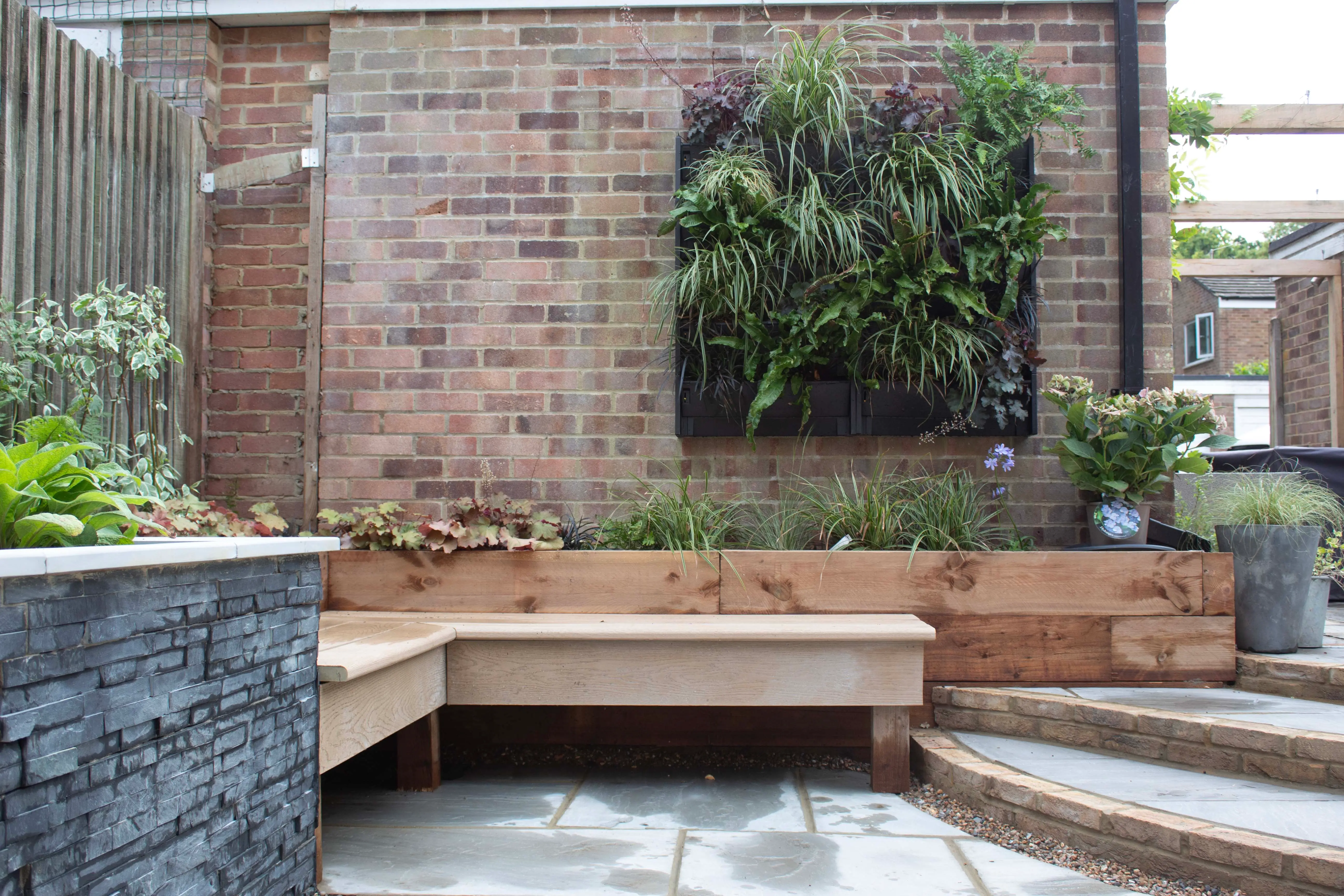 A modern outdoor space featuring a wooden bench, brick wall, and greenery, creating a serene atmosphere.