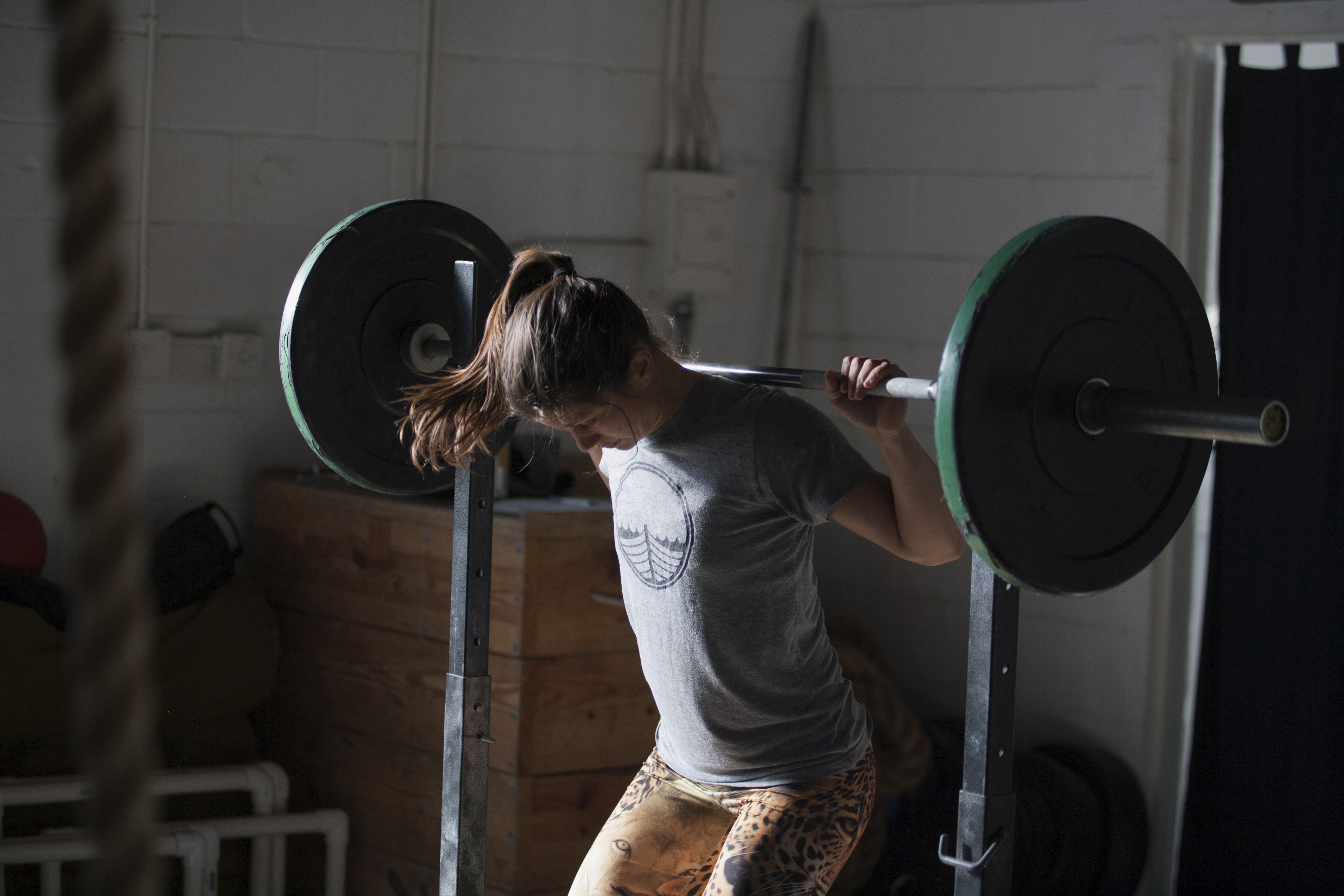 Young woman performing a squat with a heavy barbell on her shoulders in a gym, focusing on maintaining form during a strength training workout.