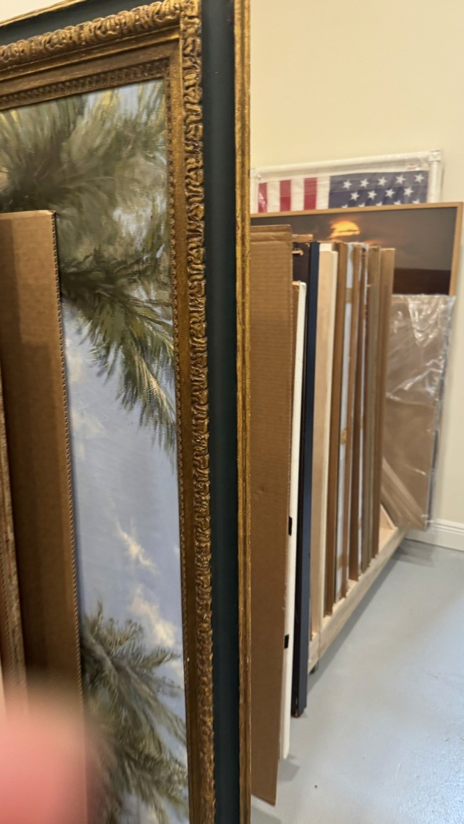 Framed artwork storage rack holding a palm tree painting and an American flag print