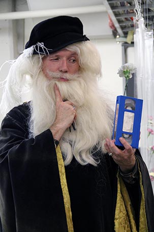 portrait of a man with a black cloth and white long hair and beard holding a videotape in his hand