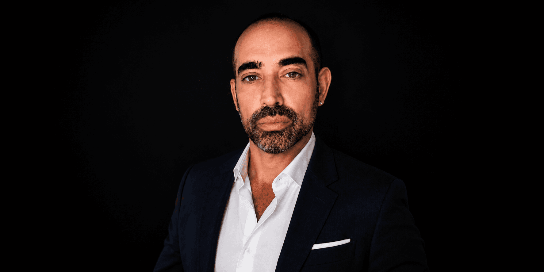 Erik Leitzes wearing a navy suit and white shirt against a black studio background.