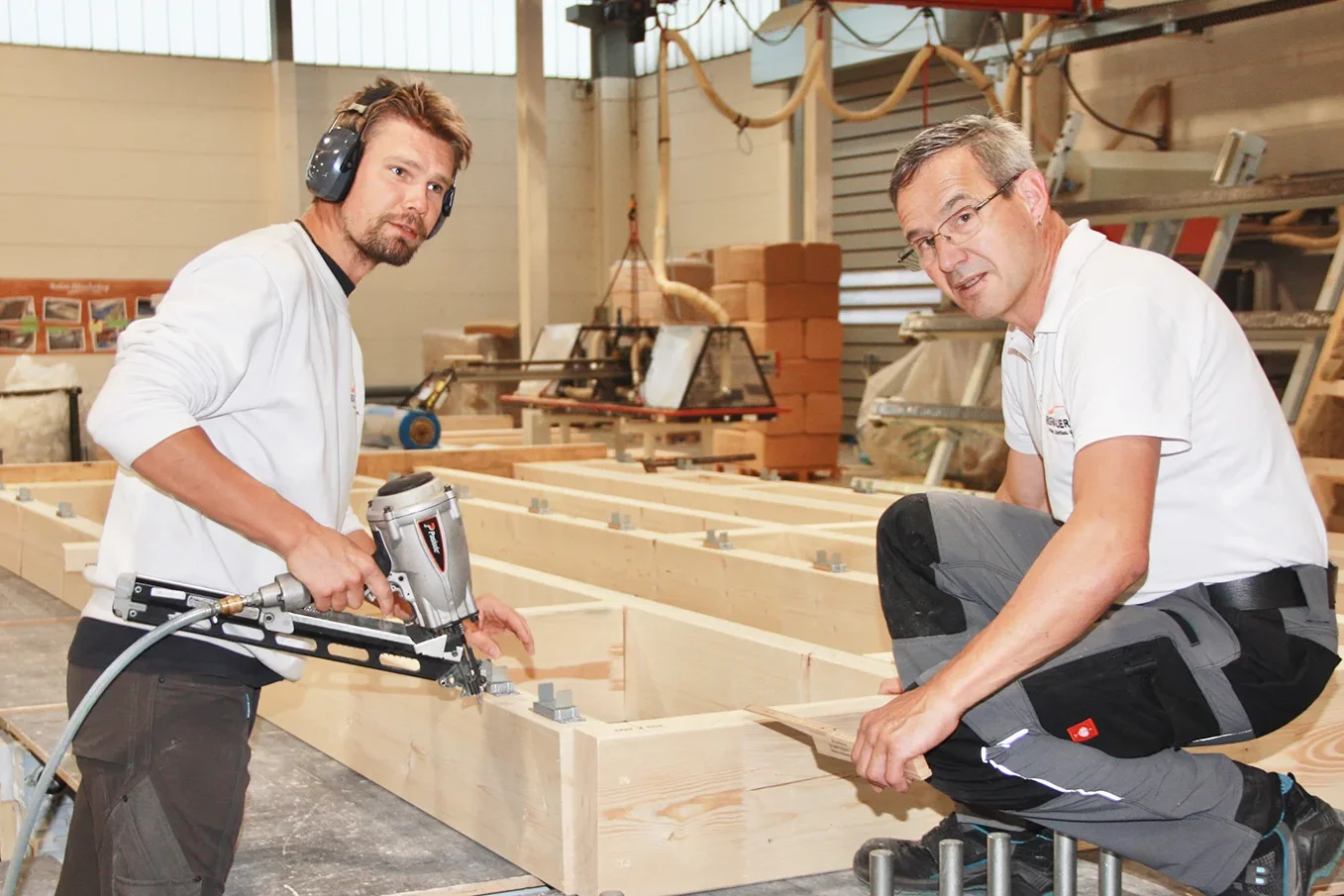 Zwei Handwerker im Metallwerk bearbeiten Holzkonstruktionen des Holzbaus mit Nägeln und Werkzeugen.